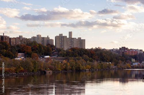 Fototapeta Naklejka Na Ścianę i Meble -  cityscape view of the North Bronx from across the Harlem River at the golden hour, with fall foliage and twilight clouds in the sky