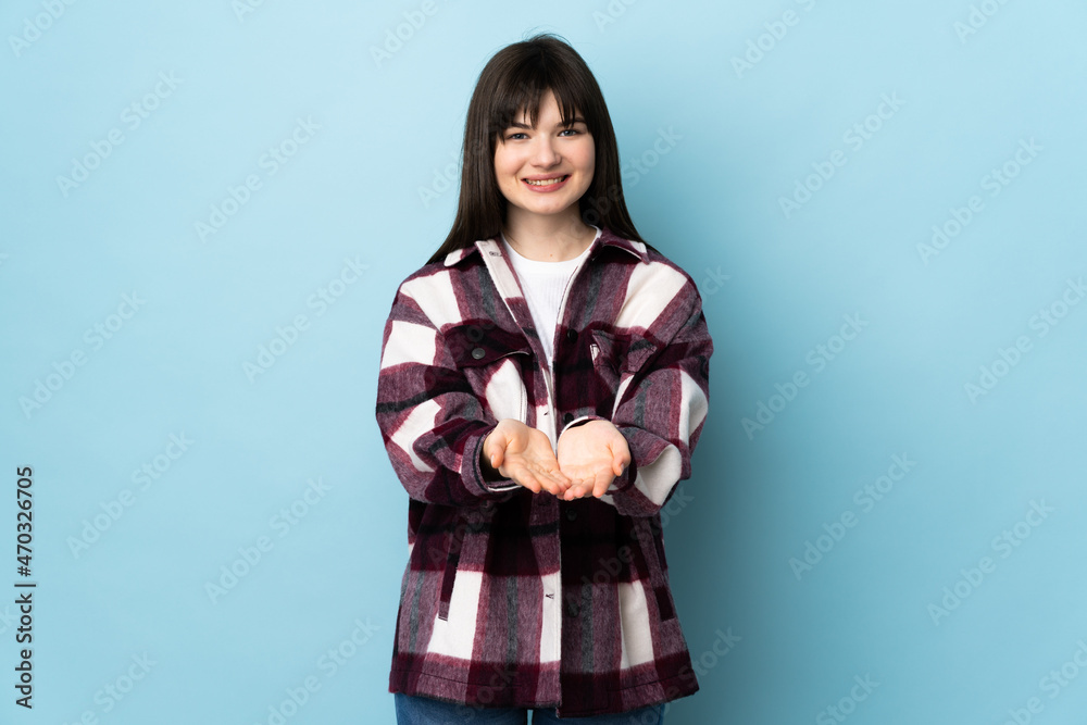Teenager Ukrainian girl isolated on blue background holding copyspace imaginary on the palm to insert an ad Teenager Ukrainian girl isolated on blue background holding copyspace imaginary on the palm to insert an ad