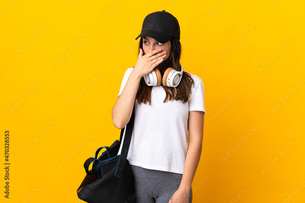 Obraz premium Young sport woman with sport bag isolated on yellow background doing surprise gesture while looking to the side