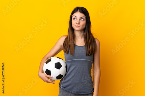 Young football player woman isolated on yellow background and looking up © luismolinero