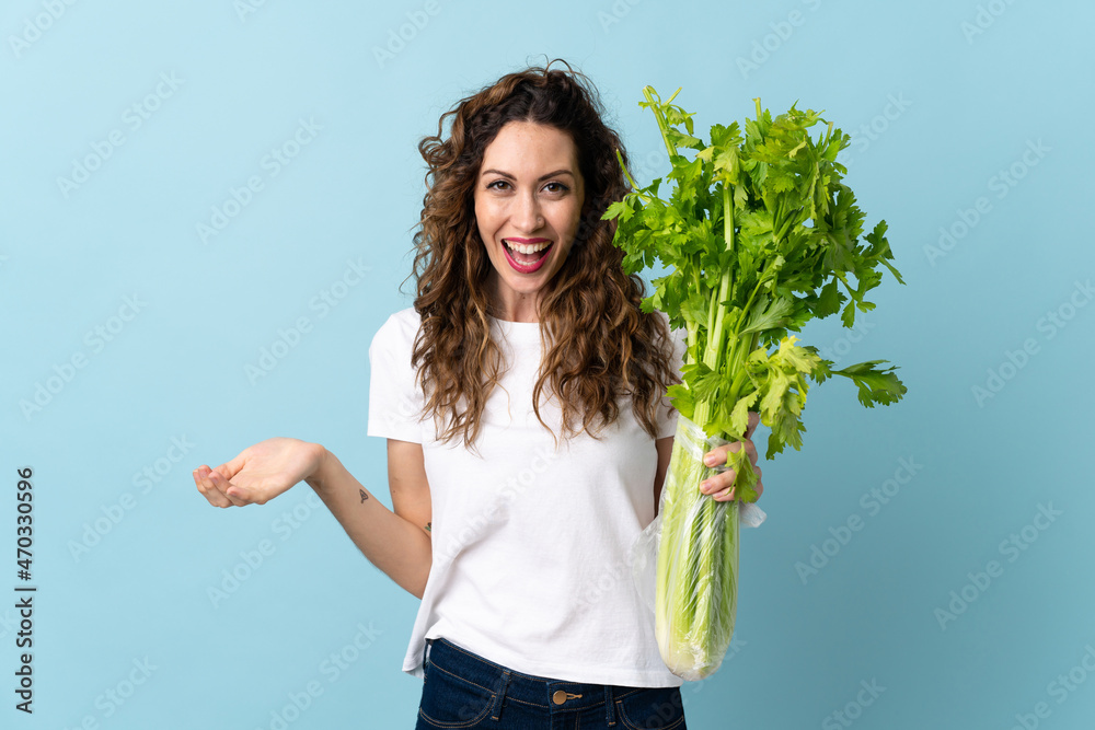Young woman holding a celery isolated on blue background with shocked facial expression Young woman holding a celery isolated on blue background with shocked facial expression