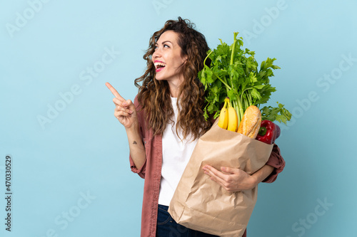 Young woman holding a grocery shopping bag isolated on blue background intending to realizes the solution while lifting a finger up