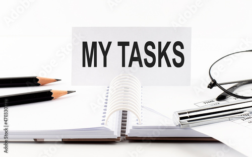 Text MY TASKS on paper card,pen, pencils, glasses,financial documentation on table - business concept