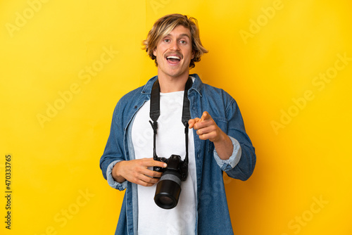 Young photographer man isolated on yellow background surprised and pointing front