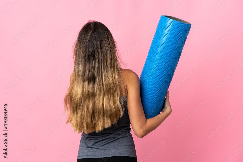 Young sport woman going to yoga classes while holding a mat isolated on pink background in back position Young sport woman going to yoga classes while holding a mat isolated on pink background in back position