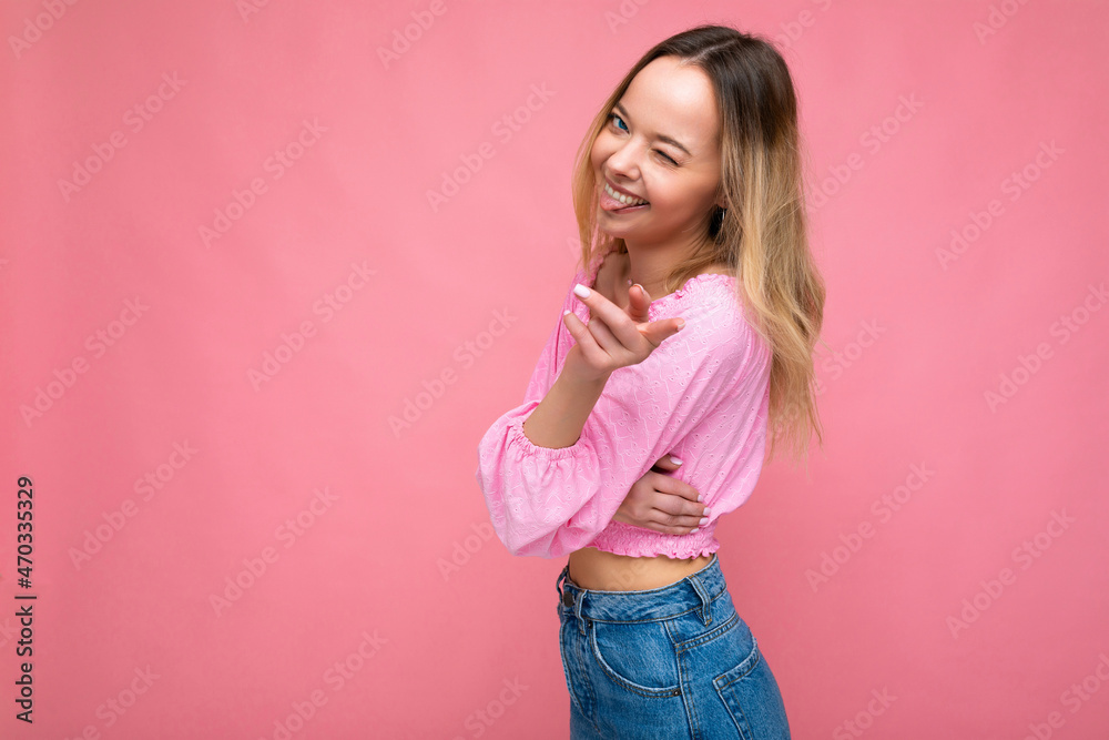 Photo shot of young beautiful cute happy blonde woman wearing stylish pink crop top isolated over pink background with copy space