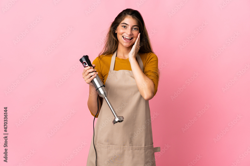 Young chef woman using hand blender isolated on pink background shouting with mouth wide open Young chef woman using hand blender isolated on pink background shouting with mouth wide open