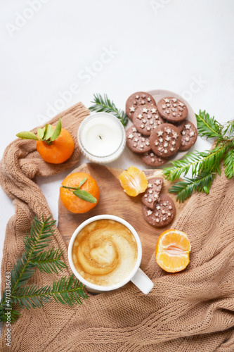 Big cup of coffee with milk, clementine and chocolate cookies on the white bedsheet. Fir tree branches around coffee and dessert. Christmas, new year mood composition. Holiday morning time. Template.