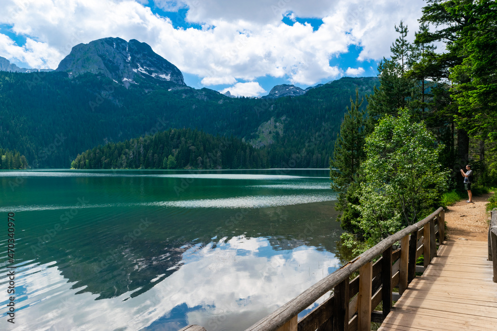 Tourist man on wooden footbridge over stream and Glacial Black Lake. Durmitor National Park. Montenegro.