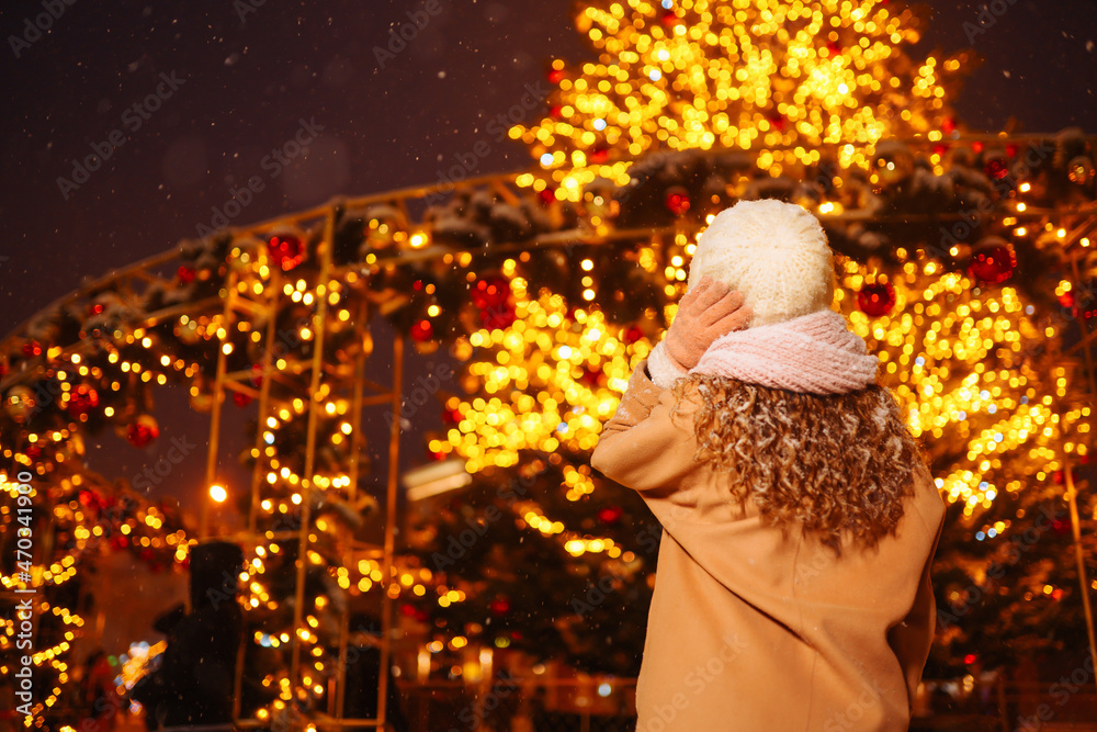 Young woman in winter style clothes against the backdrop of garland lights in the evening. Cold weather. Winter fashion, holidays, rest, travel concept. Young woman in winter style clothes against the backdrop of garland lights in the evening. Cold weather. Winter fashion, holidays, rest, travel concept.