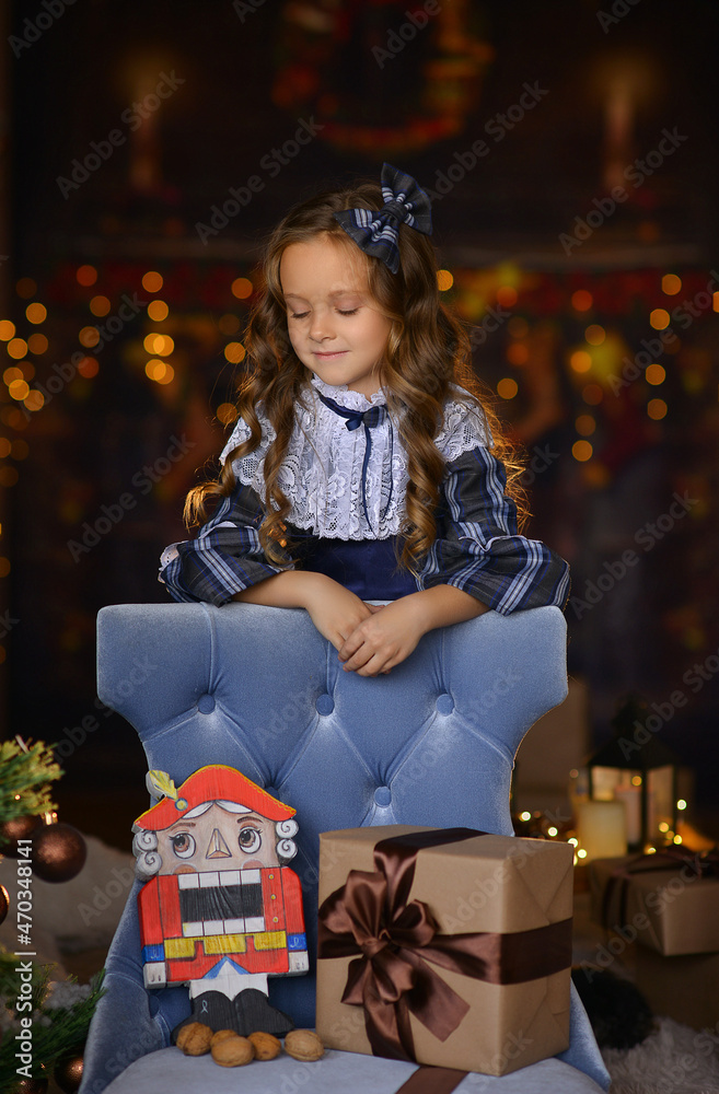 a girl in an elegant dress sits near a Christmas tree with a nutcracker