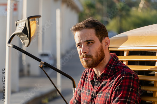 Young man in red plaid shirt and retro style leaning on the hood of a yellow bus