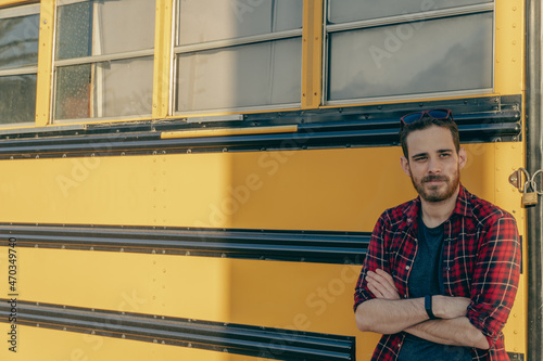 Young man in red plaid shirt and retro style with sunglasses leaning on an old yellow bus