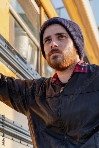 Young stylish hipster man staring down the street leaning his elbow on an old yellow bus