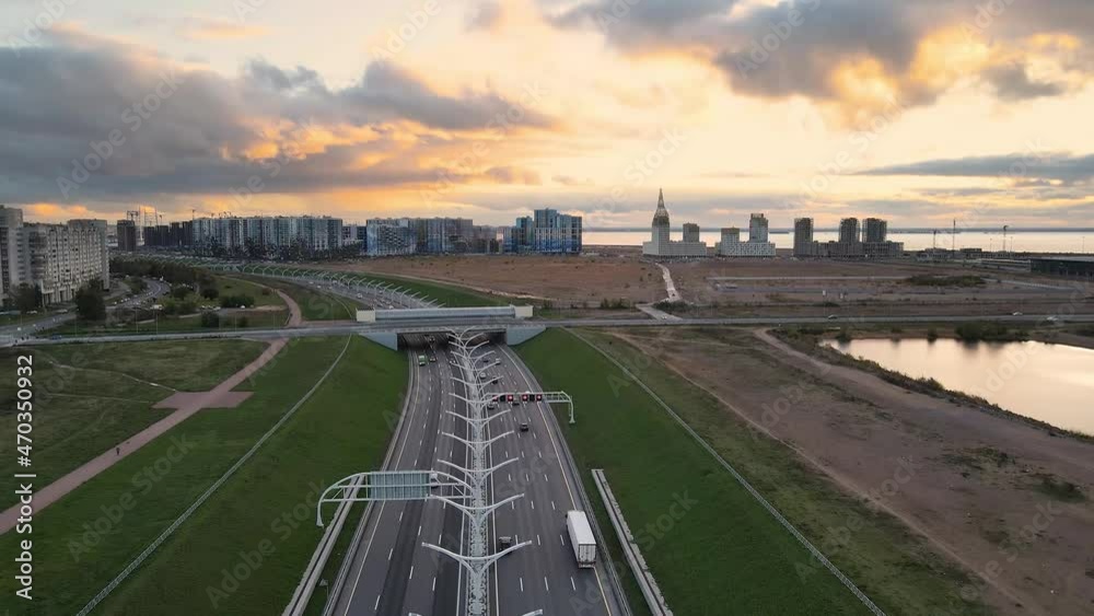Aerial fly over high speed road in city center. A lots of cars moving fast on highway. Drone is flying up. Sunset, bridge and cityscape on background. Aerial fly over high speed road in city center. A lots of cars moving fast on highway. Drone is flying up. Sunset, bridge and cityscape on background.