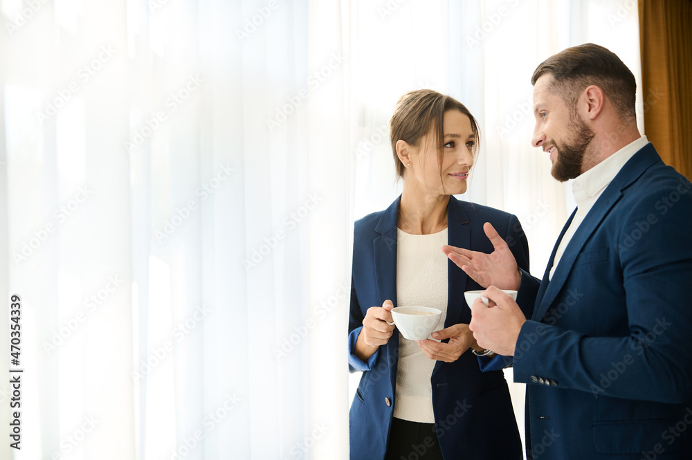 Two business partners talking to each other over a cup of coffee, standing by the window. Concept of successful negotiations, service relationship, business and partnership. Copy space for ads Two business partners talking to each other over a cup of coffee, standing by the window. Concept of successful negotiations, service relationship, business and partnership. Copy space for ads
