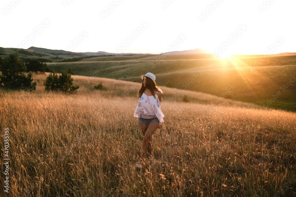 Woman walking through a field of tall grass at sunset