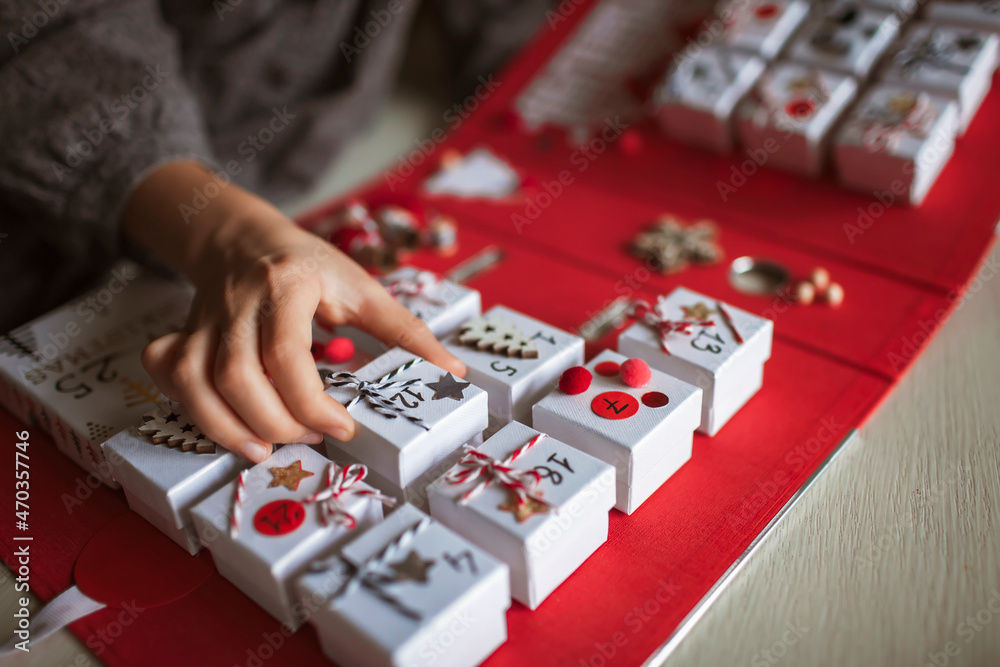 Obraz premium Pretty girl holds an original advent calendar made of jewelry boxes and a binder, New Year craft, diy. Magic of moment, seasonal activity. Christmas miracle. Soft focus, depth of field
