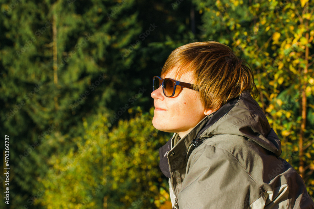 Middle-aged smiling woman wearing sunglasses enjoying sunshine at fall day in pine spruce fir green forest. Fresh air. Female traveler taking breath outdoors. Adventures journey, trip alone. Keep calm Middle-aged smiling woman wearing sunglasses enjoying sunshine at fall day in pine spruce fir green forest. Fresh air. Female traveler taking breath outdoors. Adventures journey, trip alone. Keep calm