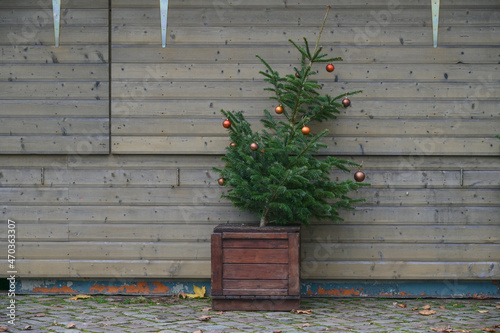 Slanted fir tree with remaining decoration stands abandoned in front of a closed booth at the Christmas market, cancelled event due to coronavirus pandemic, copy space photo