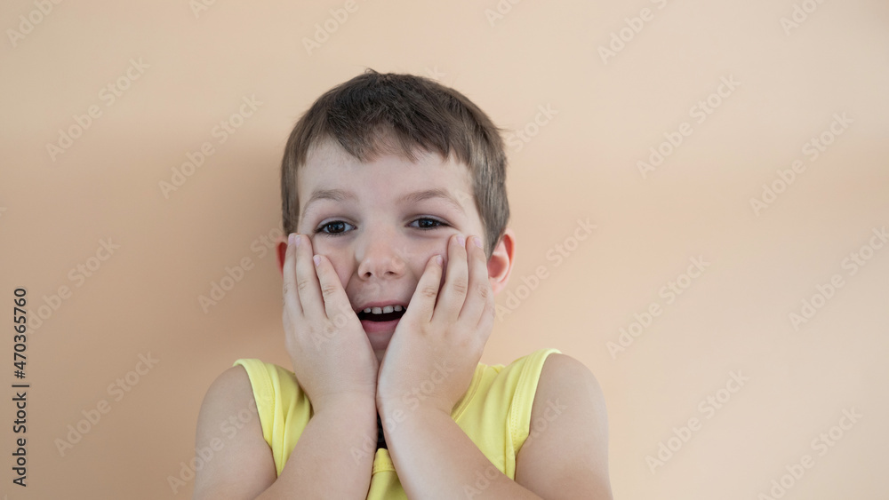 A cute boy on a light background looks surprised. Hands near the face, surprised. A cute boy on a light background looks surprised. Hands near the face, surprised.