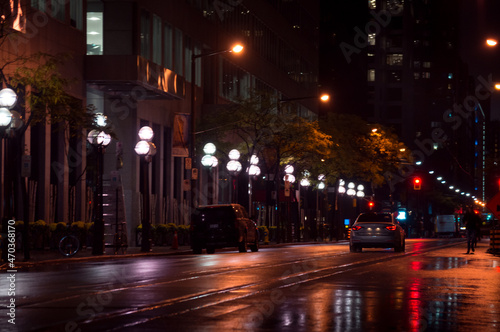 Rainy night view along a city street with a line of streetlamps, cars, light reflecting in wet asphalt surface