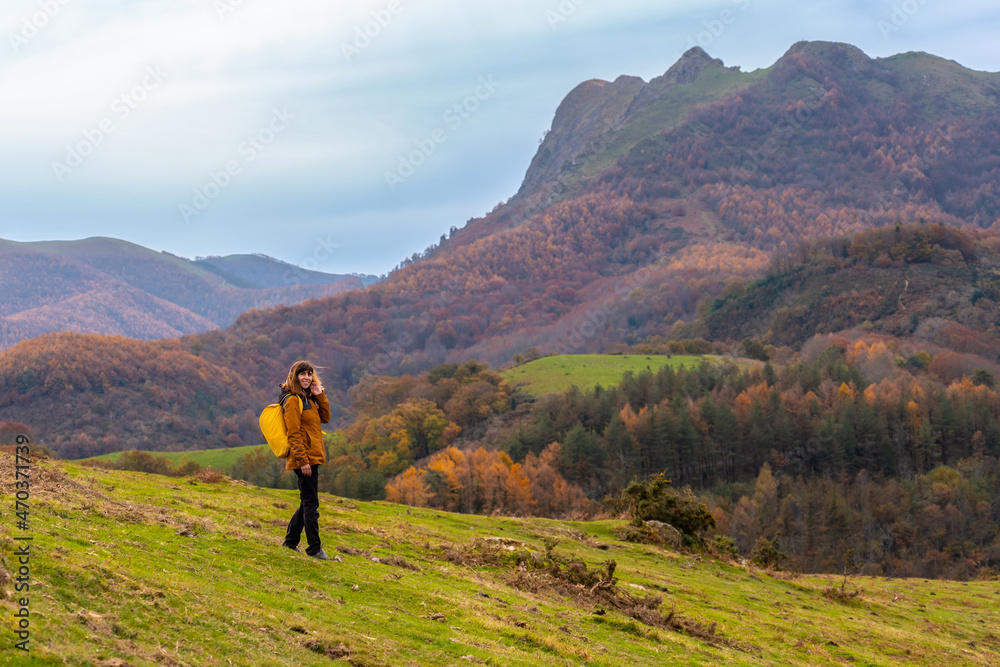 A young woman walking on top of Mount Erlaitz in autumn in the village of Irun. In the background Peñas de Aya or Aiako Harria, Gipuzkoa. Basque Country
