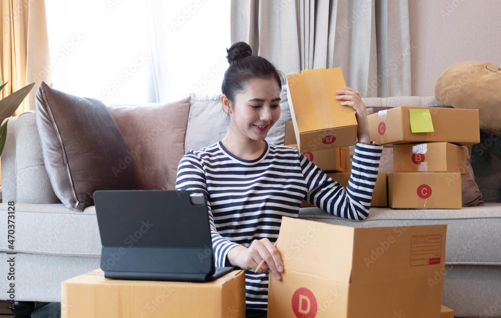 Online Marketing, Young start up small business owner writing address on cardboard box from list order. small business entrepreneur SME or freelance asian woman working with box at home Online Marketing, Young start up small business owner writing address on cardboard box from list order. small business entrepreneur SME or freelance asian woman working with box at home