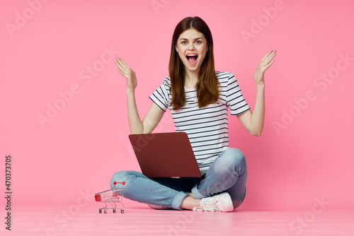 cheerful woman with laptop sitting on the floor on a pink background © VICHIZH