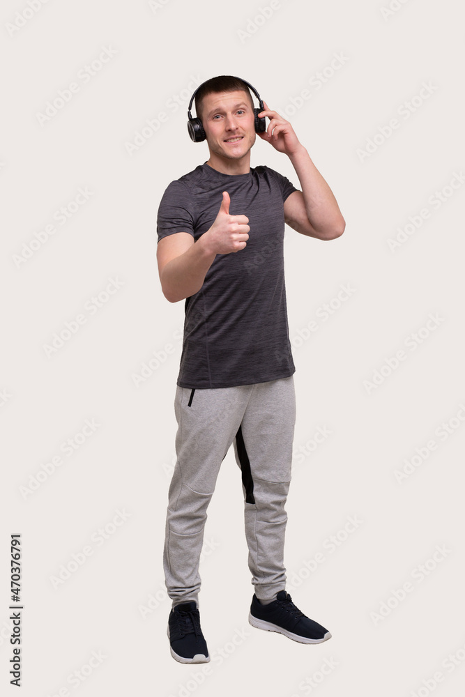 Fototapeta premium Sport Man Standing Listening to Music and Enjoys Watching to Camera Showing Thumb Up. Trainer Listening Music. Good Music. man relaxing. Music for Sport