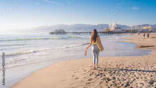 Attractive young woman walking towards Santa Monica beach pier, Los Angeles, California photo
