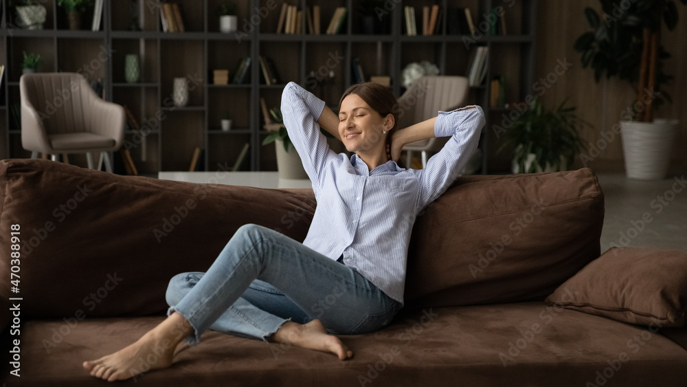 Serene young 30s woman relaxing on couch enjoy carefree weekend alone at modern cozy home. Concept of happy homeowner spend day off inside comfort apartment with air conditioner and cosy furniture Serene young 30s woman relaxing on couch enjoy carefree weekend alone at modern cozy home. Concept of happy homeowner spend day off inside comfort apartment with air conditioner and cosy furniture