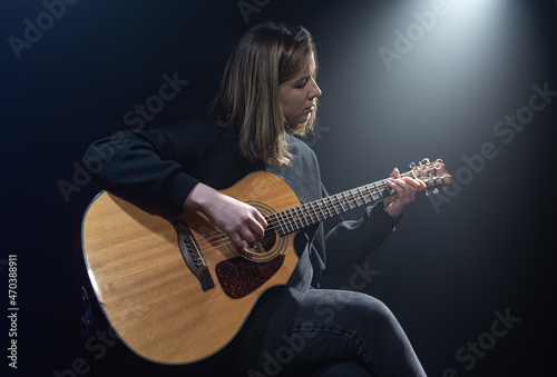 Young woman playing acoustic guitar in a dark room with haze.