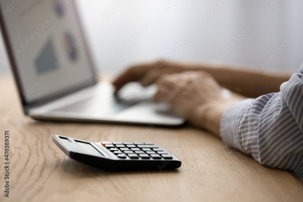 Close up focus on calculator, on background female hands on laptop keyboard, graphs charts on pc monitor. Banking, stats application services usage, investments, management of budget, finances concept Close up focus on calculator, on background female hands on laptop keyboard, graphs charts on pc monitor. Banking, stats application services usage, investments, management of budget, finances concept
