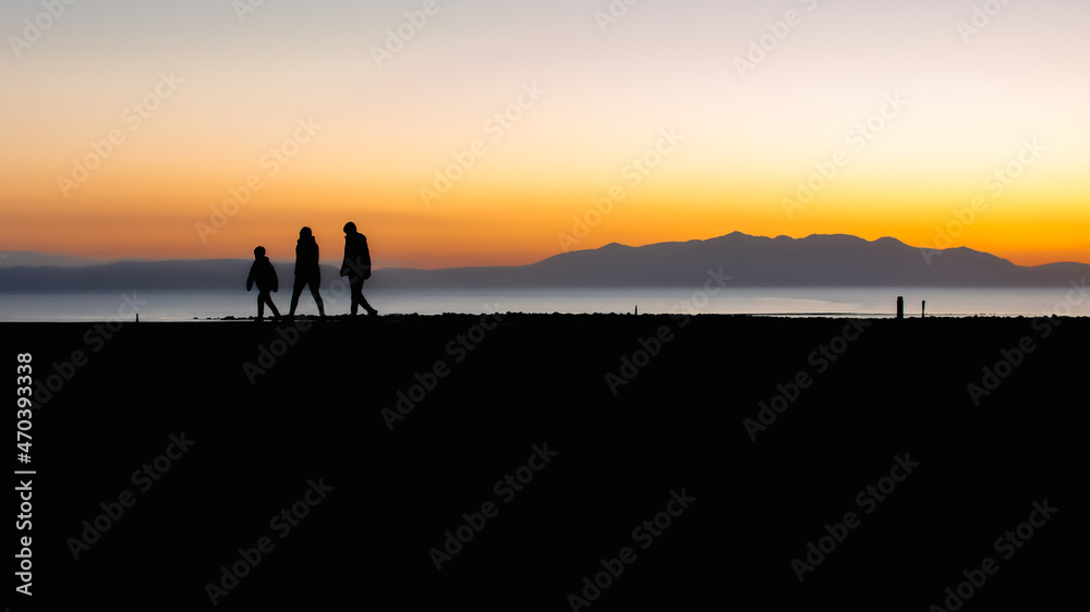 Sunset Silhouette of family walking with Arran on the horizon, Scotland