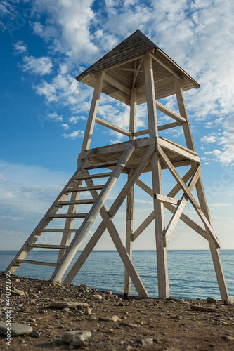 An empty lifeguard tower against the background of the sea and the blue sky with clouds. White wooden lifeguard station on the sea beach. View from below. © VeNN