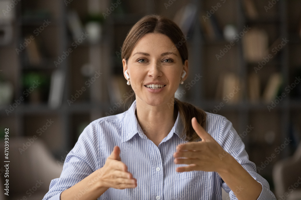 Head shot attractive businesswoman sit indoor looks at camera talks through video call. Female counsellor wear wireless earphones provide support help to client remotely. Virtual meeting event concept