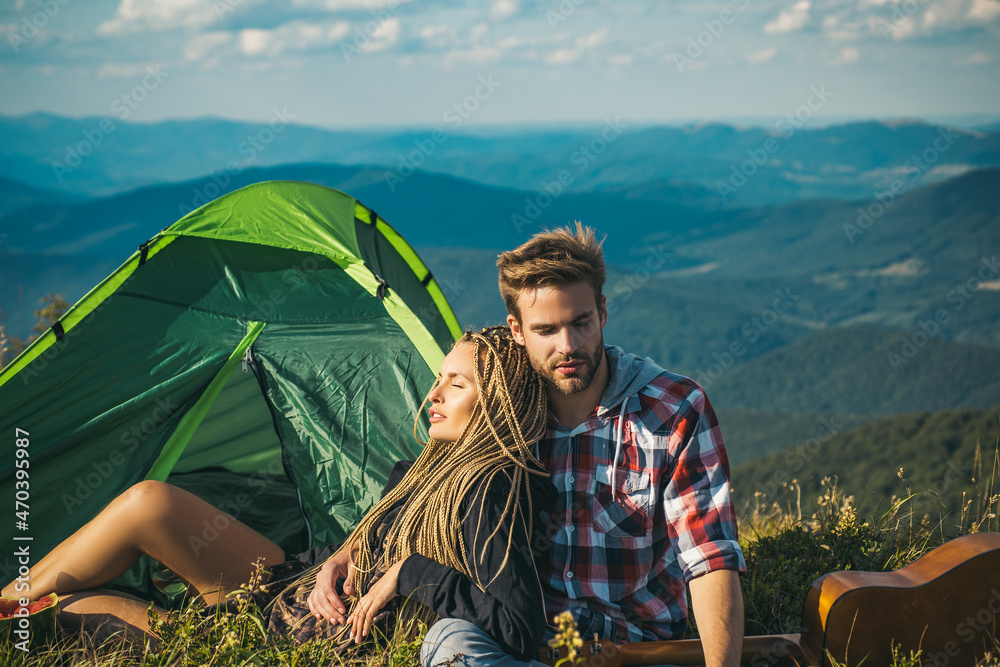 Romantic couple camping outdoors and sitting near tent. Happy Man and woman on a romantic camping vacation. Young couple in love hug each other.