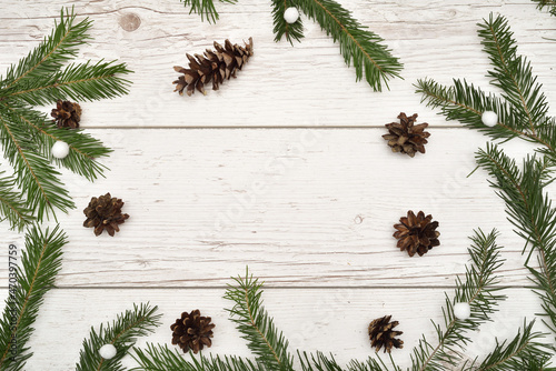 Christmas rustic wooden background with fir branches, pine cones and little white snowball ornaments. Christmas greeting card with copy space. Top view. 