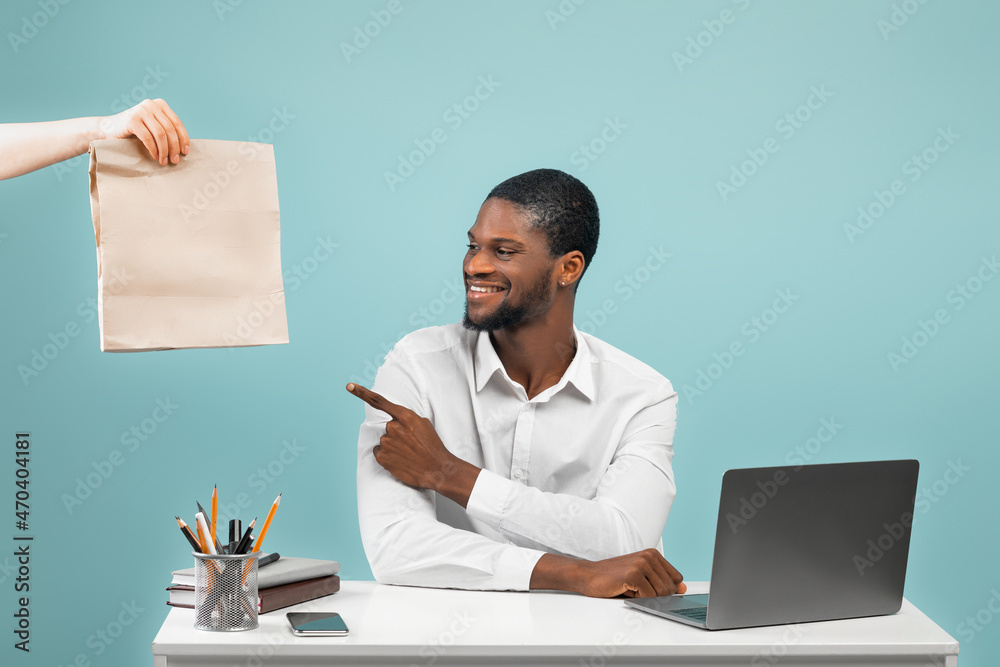 African american company worker receiving food delivery from courier and pointing on paper bag, blue background African american company worker receiving food delivery from courier and pointing on paper bag, blue background