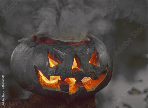 Halloween. A pumpkin on the background of a pond, it glows, a fiery flame burns inside it. The concept of the holiday of the night of all saints and scary dark fairy tales in the autumn harvest season