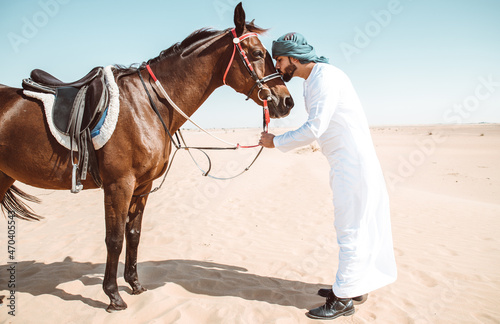 Young adult with Kandura, the emirates traditional clothes, riding his horse in the desert