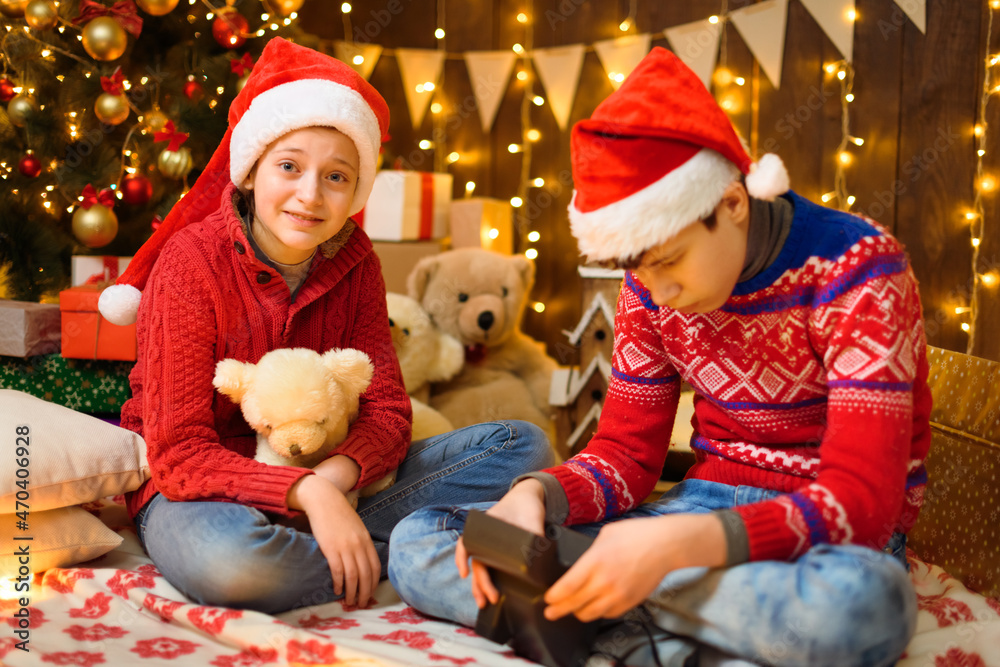 Portrait of a boy and a girl in New Year decoration. They play and take pictures. Festive lights, gifts and a Christmas tree decorated with toys. Portrait of a boy and a girl in New Year decoration. They play and take pictures. Festive lights, gifts and a Christmas tree decorated with toys.