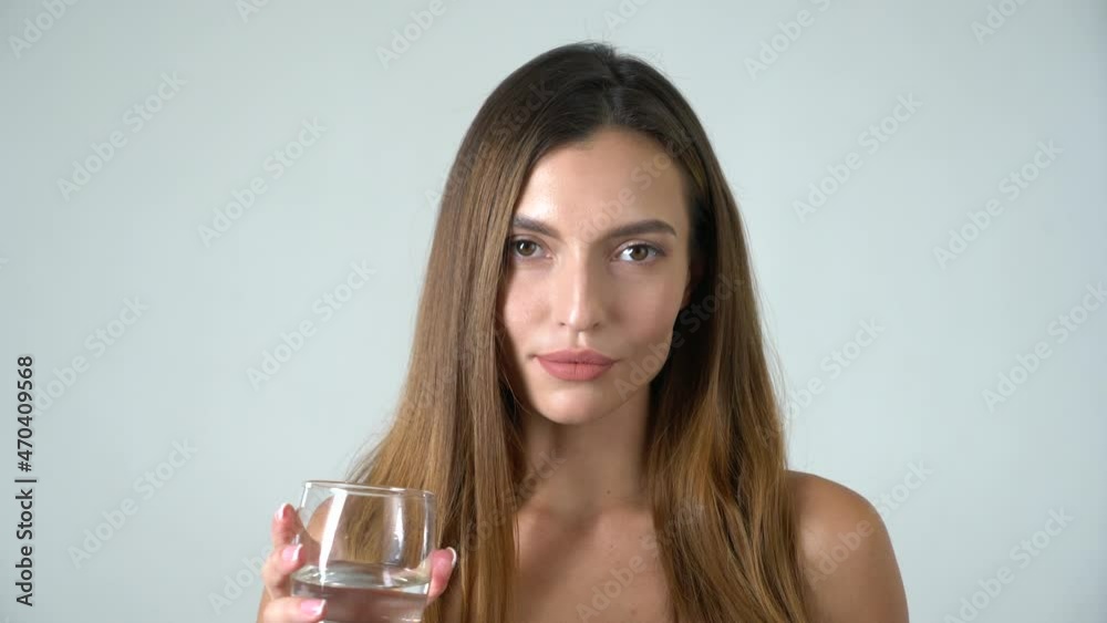 Young attractive caucasian female model drinks water and looks into camera white background Young attractive caucasian female model drinks water and looks into camera white background