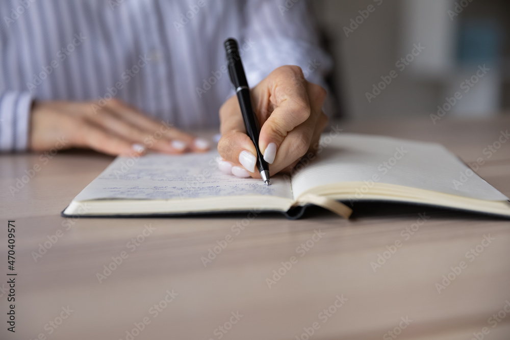 Close up young business woman handwriting notes in paper planner, managing working tasks or optimizing schedule. Skilled millennial female student learning or preparing for exam, sitting at table. Close up young business woman handwriting notes in paper planner, managing working tasks or optimizing schedule. Skilled millennial female student learning or preparing for exam, sitting at table.