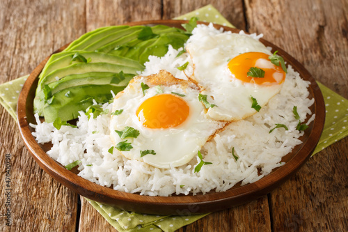 Boiled rice on top with fried eggs served with fresh avocado close-up in a plate on the table. horizontal