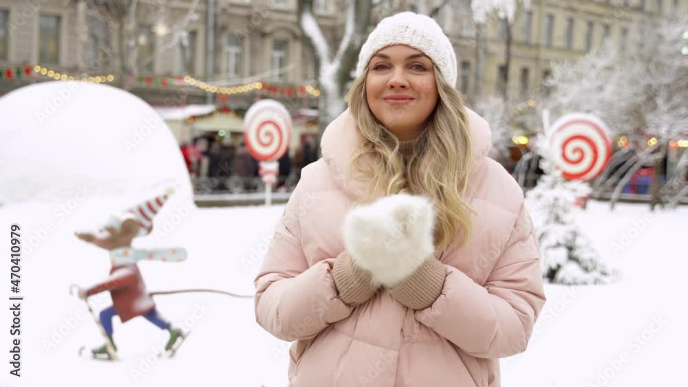 beautiful young woman stands and claps her palms in warm white fluffy mittens on a snowy city street beautiful young woman stands and claps her palms in warm white fluffy mittens on a snowy city street