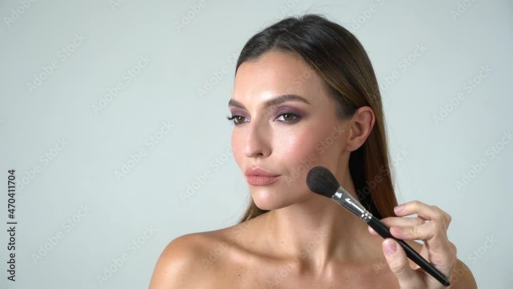 Makeup artist put make-up to the gorgeous face of beautiful european model closeup in white background Makeup artist put make-up to the gorgeous face of beautiful european model closeup in white background