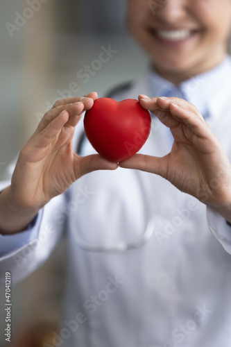 Vertical crop close up smiling Indian woman doctor cardiologist holding red heart in hands, medical insurance and cardiovascular disease prevention concept, professional cardiology service