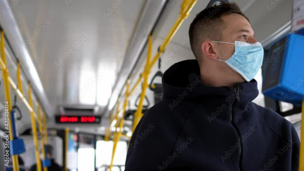 Close up portrait of a man in a medical mask with a qr code, staying in public transport with a smartphone in his hands. There are few passengers on the shuttle bus. Close up portrait of a man in a medical mask with a qr code, staying in public transport with a smartphone in his hands. There are few passengers on the shuttle bus.